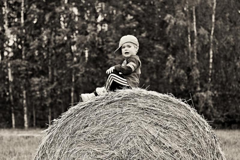 A young boy on top of the hay roll